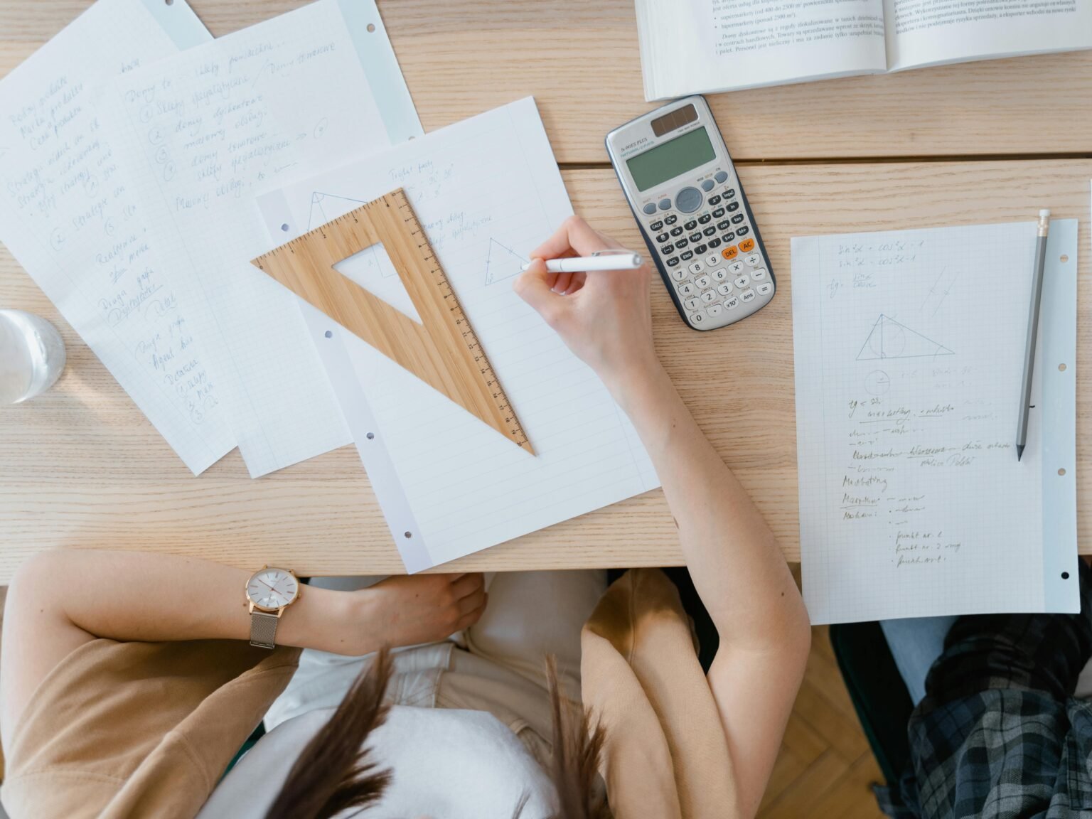 Des exercices de mathématiques, une équerre et une calculatrice posés sur une table
